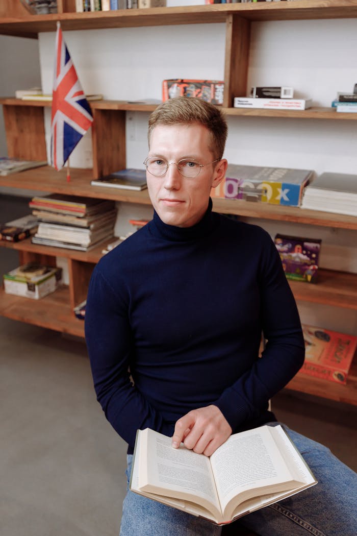 Caucasian man in eyeglasses reading a book in a cozy library space.